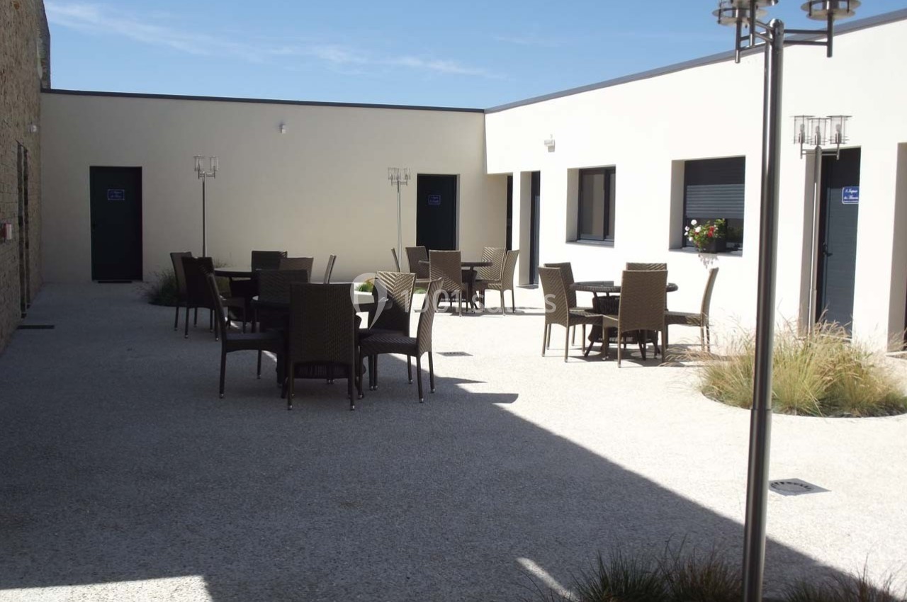 Cour intérieure avec mobilier de jardin en rotin, entourée de murs clairs et éclairée par un ciel dégagé.