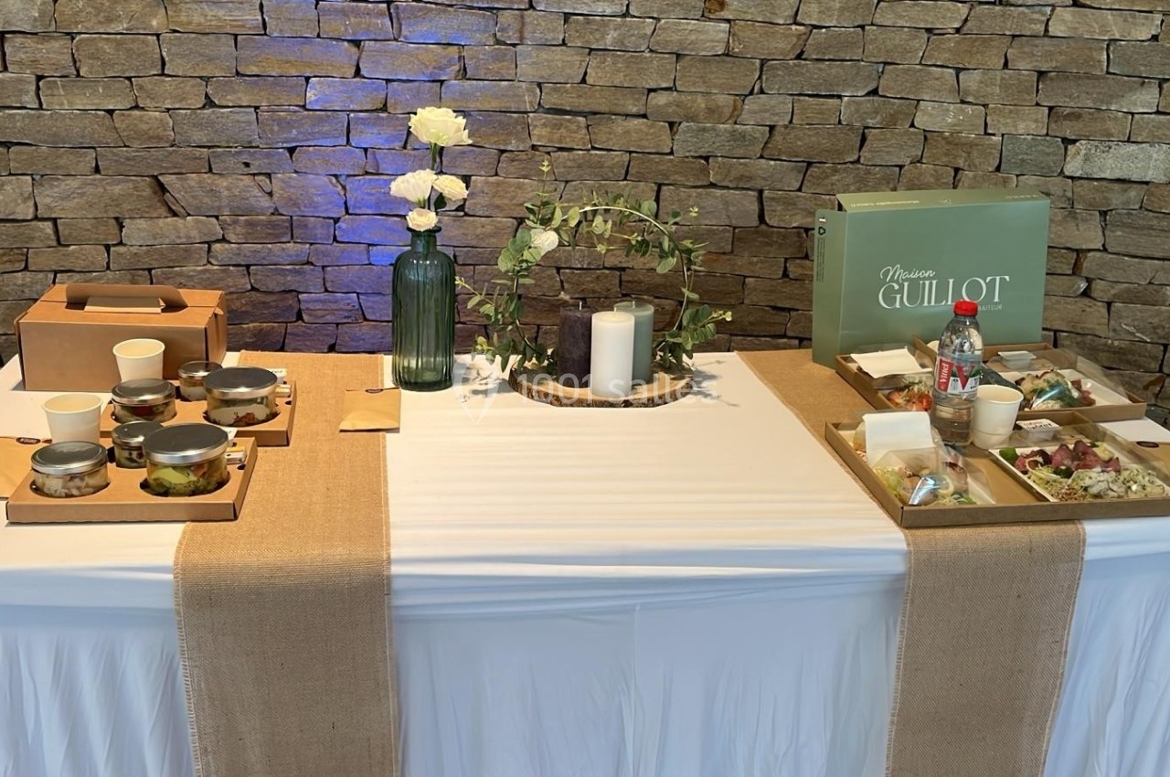 Table dressée avec nappes blanches, décor rustique, plats individuels, boissons et éléments de décoration florale.