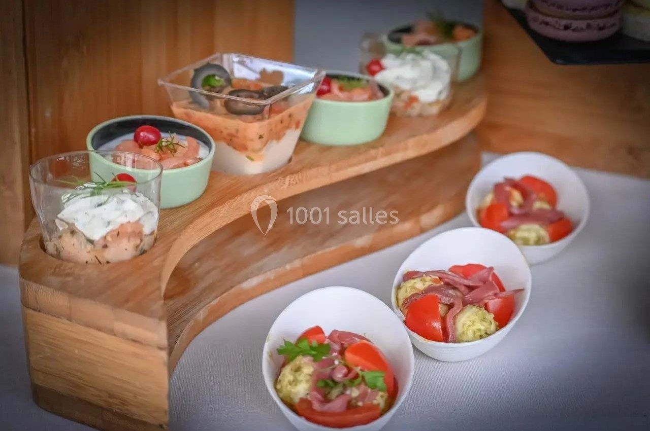 Assortiment de verrines et bols contenant des préparations salées avec légumes, fromage et herbes sur un présentoir en bois.