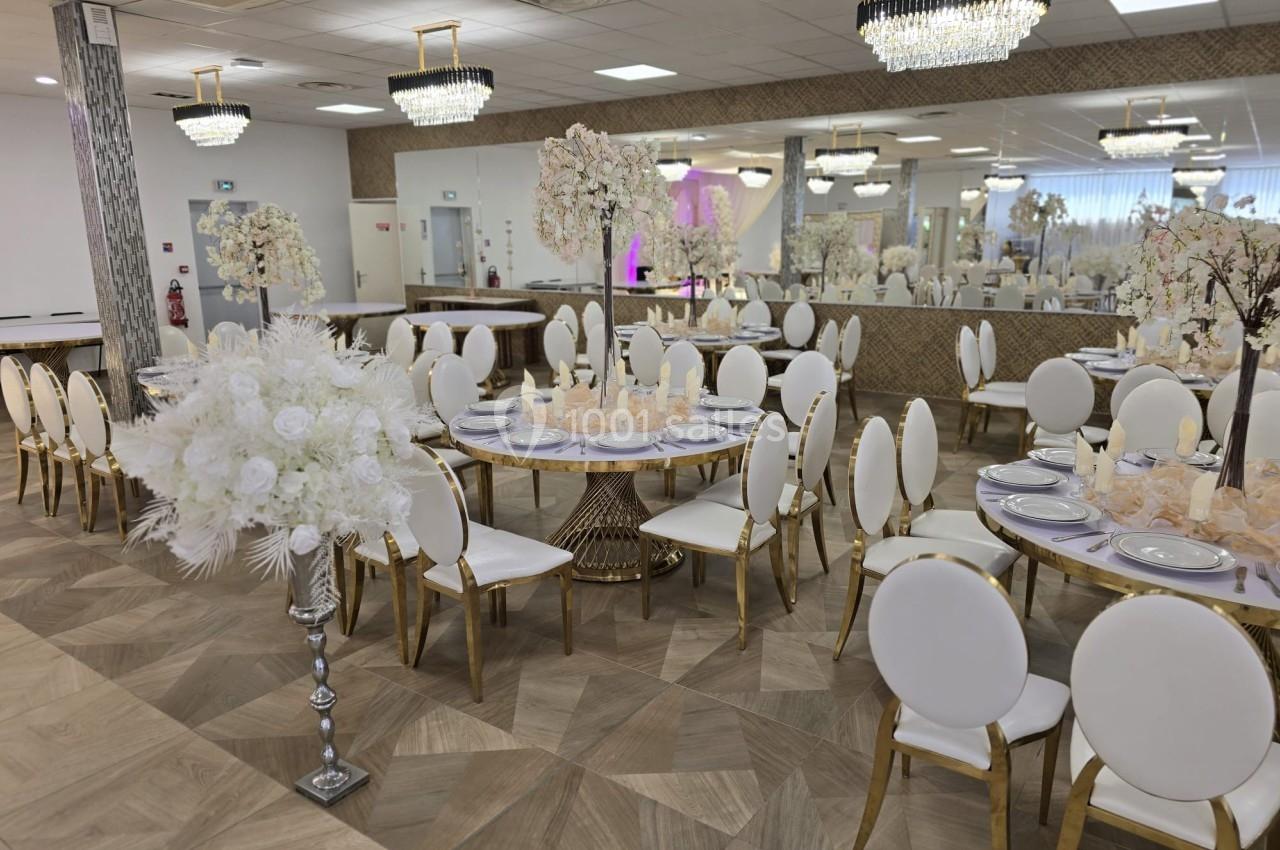 Salle de réception élégante avec tables décorées, chaises blanches et dorées, miroirs et lustres modernes.