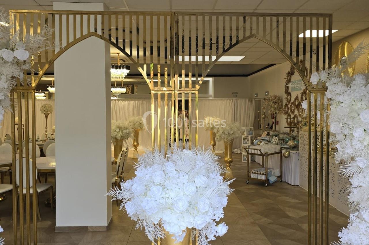 Décoration intérieure élégante avec des arches dorées, des fleurs blanches et un espace aménagé pour un événement.