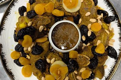 Assiette garnie d'un jarret d'agneau en sauce, accompagnée de légumes, fruits confits et d'une décoration en œuf et cerise.