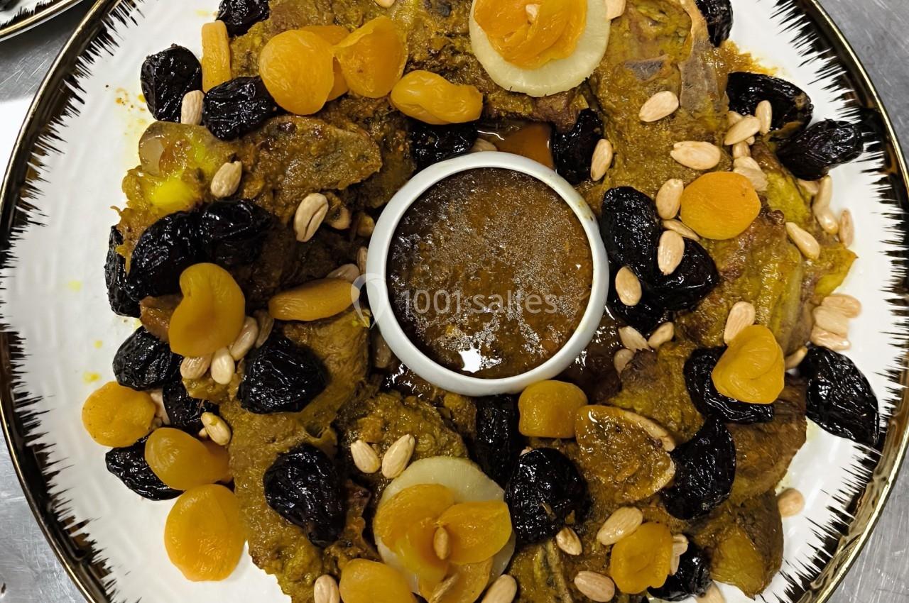 Plat de viande accompagné de pruneaux, abricots secs, amandes et sauce au centre, présenté sur une assiette blanche.