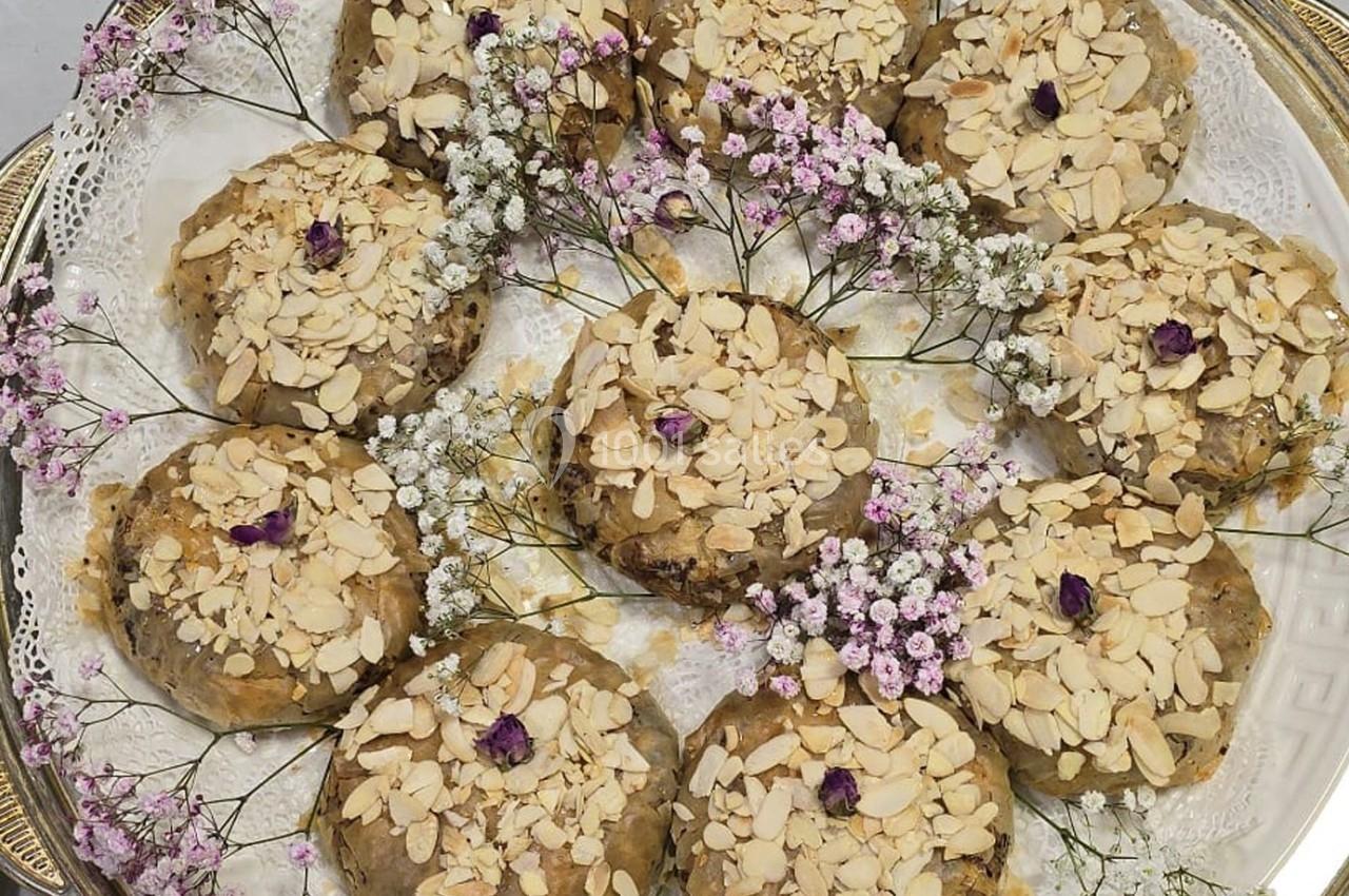 Assortiment de pâtisseries garnies d'amandes effilées et décorées de petites fleurs sur un plateau orné de dentelle.