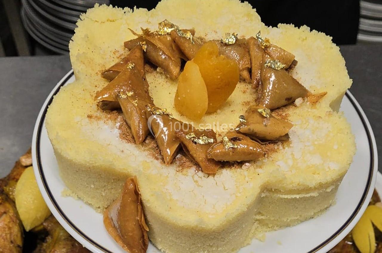 Assiette de semoule dressée en forme de fleur, garnie de fruits secs, feuilles d'or et poudre de cannelle.