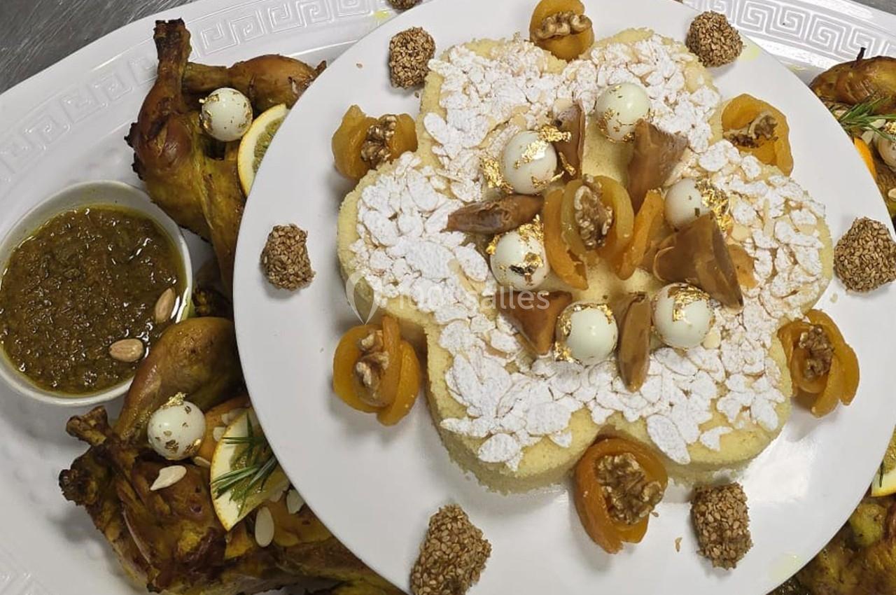 Plat de semoule décoré d'amandes, abricots secs et noix, accompagné de poulet rôti et sauce aux herbes.