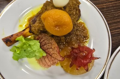 Assiette garnie d'un jarret d'agneau en sauce, accompagnée de légumes, fruits confits et d'une décoration en œuf et cerise.