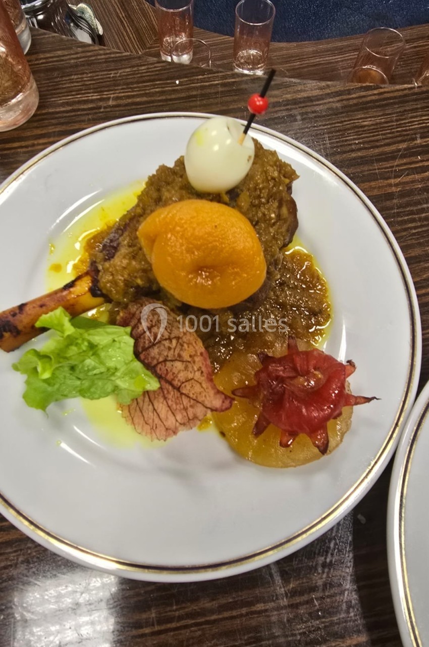 Assiette garnie d'un jarret d'agneau en sauce, accompagnée de légumes, fruits confits et d'une décoration en œuf et cerise.