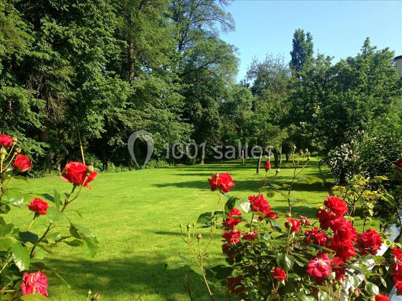 Pelouse verdoyante bordée d'arbres et de buissons fleuris avec des roses rouges au premier plan.