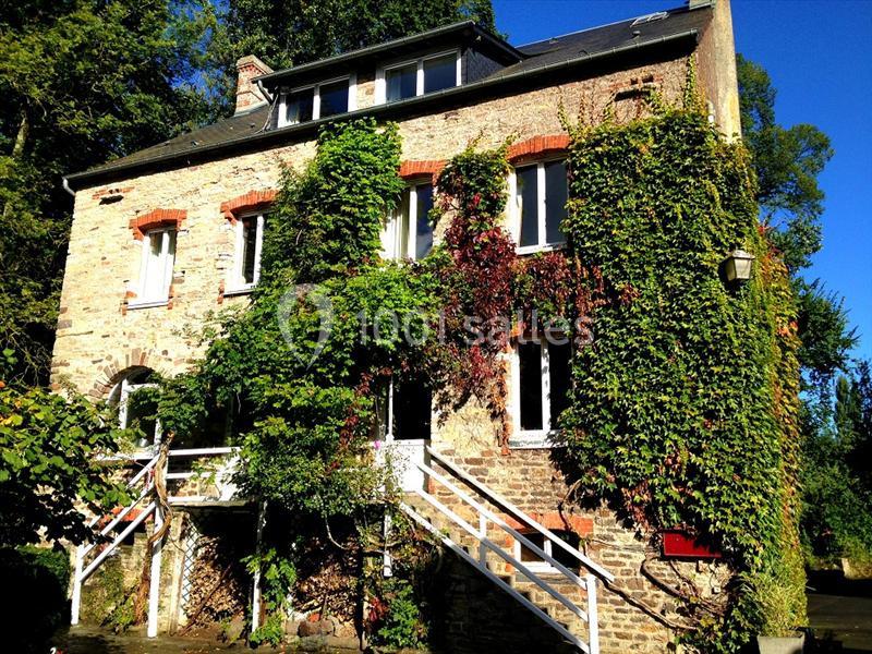 Façade d'une maison en pierre recouverte de végétation, avec escaliers blancs et entourée d'arbres.