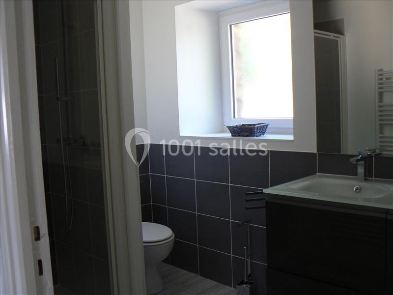 Salle de bain moderne avec carrelage gris, lavabo, toilettes et fenêtre laissant entrer la lumière naturelle.