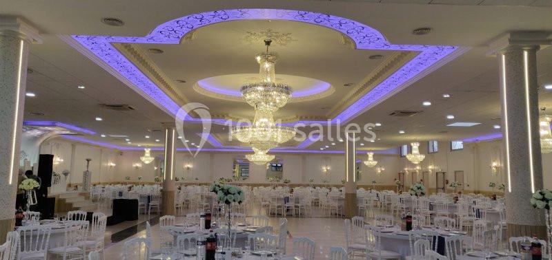 Salle de réception élégante avec lustres imposants, éclairage violet et tables dressées pour un événement.