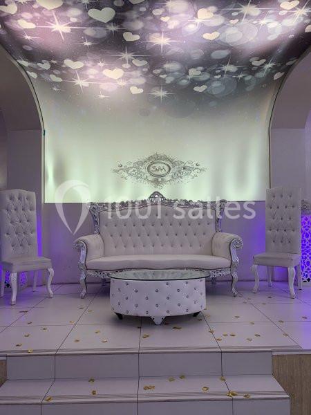 Canapé blanc capitonné avec deux fauteuils assortis, table basse ronde, décor lumineux avec motifs de cœurs et étoiles.