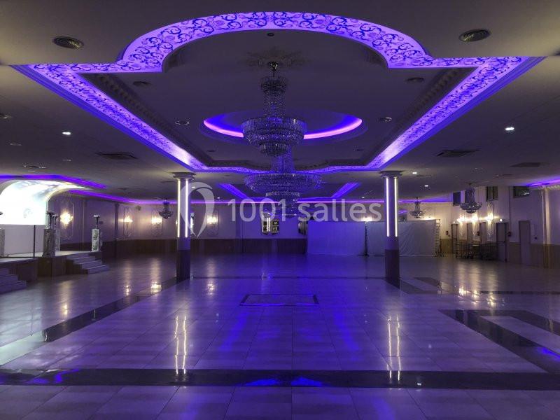 Salle de réception spacieuse avec éclairage violet, lustres suspendus et sol en carrelage brillant.