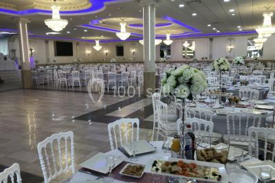 Salle de réception décorée avec tables dressées, compositions florales, buffet, plats servis et pièce montée.