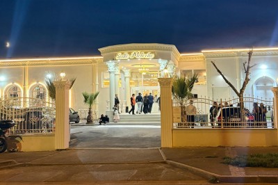 Façade d'un bâtiment blanc avec des arches vitrées, un escalier central et un parking vide à l'avant.