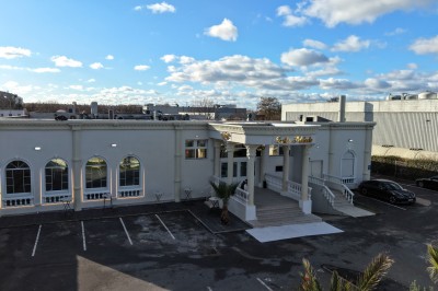 Façade d'un bâtiment blanc avec des arches vitrées, un escalier central et un parking vide à l'avant.