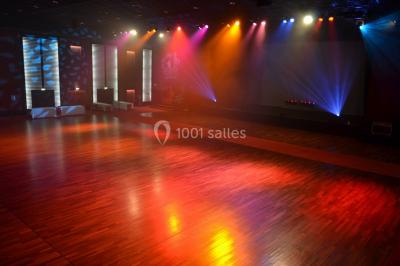 Salle de réception avec tables dressées, verres alignés au premier plan et décorations florales en arrière-plan.