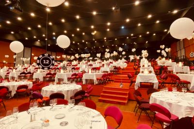 Salle de réception avec tables dressées, verres alignés au premier plan et décorations florales en arrière-plan.