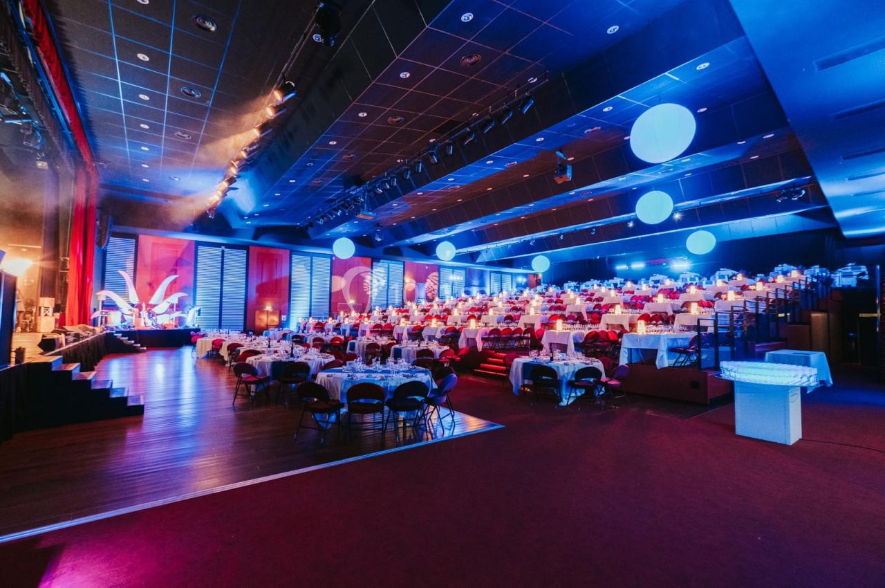 Salle de réception éclairée en bleu avec des tables dressées et une scène au fond.