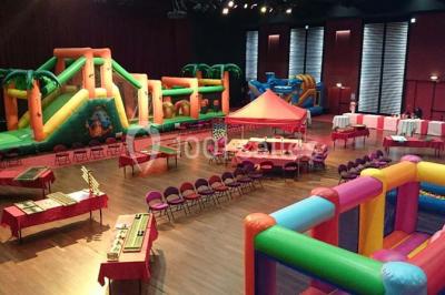 Salle avec structures gonflables colorées, tables, chaises et stands installés pour un événement intérieur.