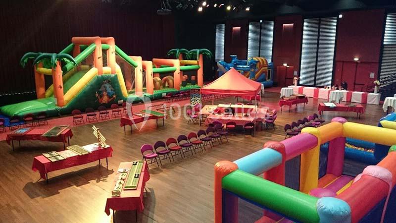 Salle avec structures gonflables colorées, tables, chaises et stands installés pour un événement intérieur.