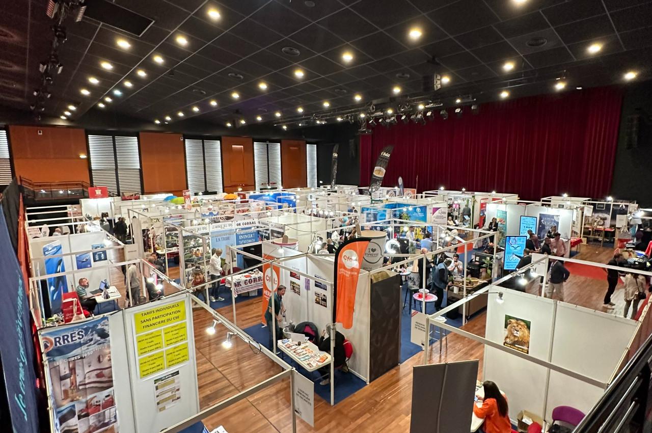 Vue plongeante sur un salon professionnel avec des stands alignés, des visiteurs et une salle éclairée.