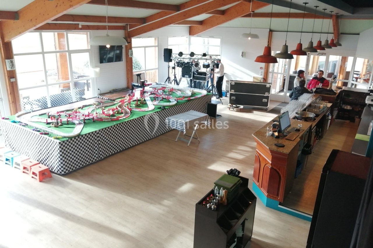 Salle lumineuse avec un circuit de voitures miniatures, un bar en bois et des équipements techniques en arrière-plan.