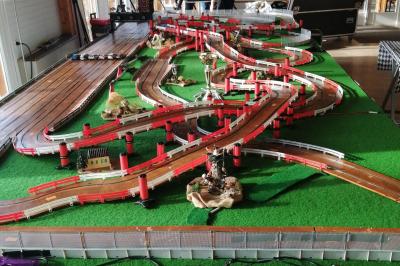 Circuit de course miniature avec des pistes sinueuses, des décors et des structures sur une table dans une salle.