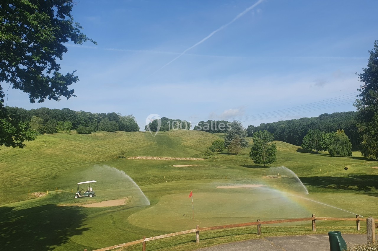 Arrosage automatique d'un terrain de golf verdoyant sous un ciel dégagé, avec un arc-en-ciel visible près du green.