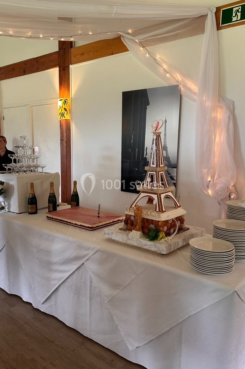 Pièce montée en forme de tour Eiffel sur une table décorée, entourée de bouteilles de champagne et d'assiettes empilées.