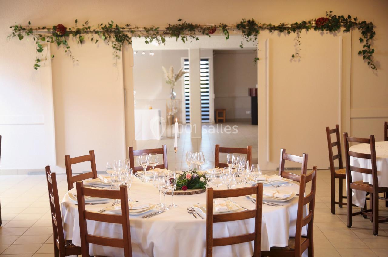 Salle de réception décorée avec des tables rondes dressées, nappes blanches et guirlande végétale suspendue.