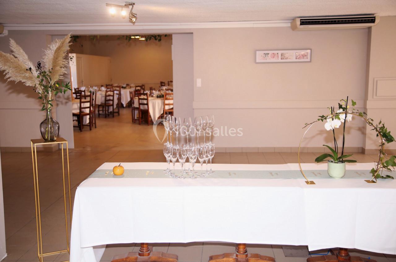 Table décorée avec des verres à pied, fleurs et pampas, dans une salle de réception lumineuse avec des tables dressées au…
