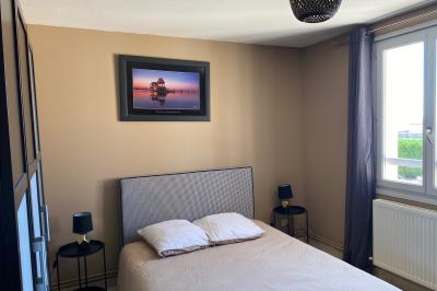 Chambre lumineuse avec lit double, armoire, téléviseur sur table et fenêtre donnant sur un extérieur verdoyant.