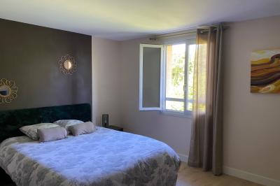 Chambre lumineuse avec lit double, armoire, téléviseur sur table et fenêtre donnant sur un extérieur verdoyant.