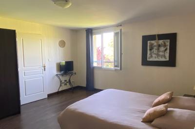 Chambre lumineuse avec lit double, armoire, téléviseur sur table et fenêtre donnant sur un extérieur verdoyant.