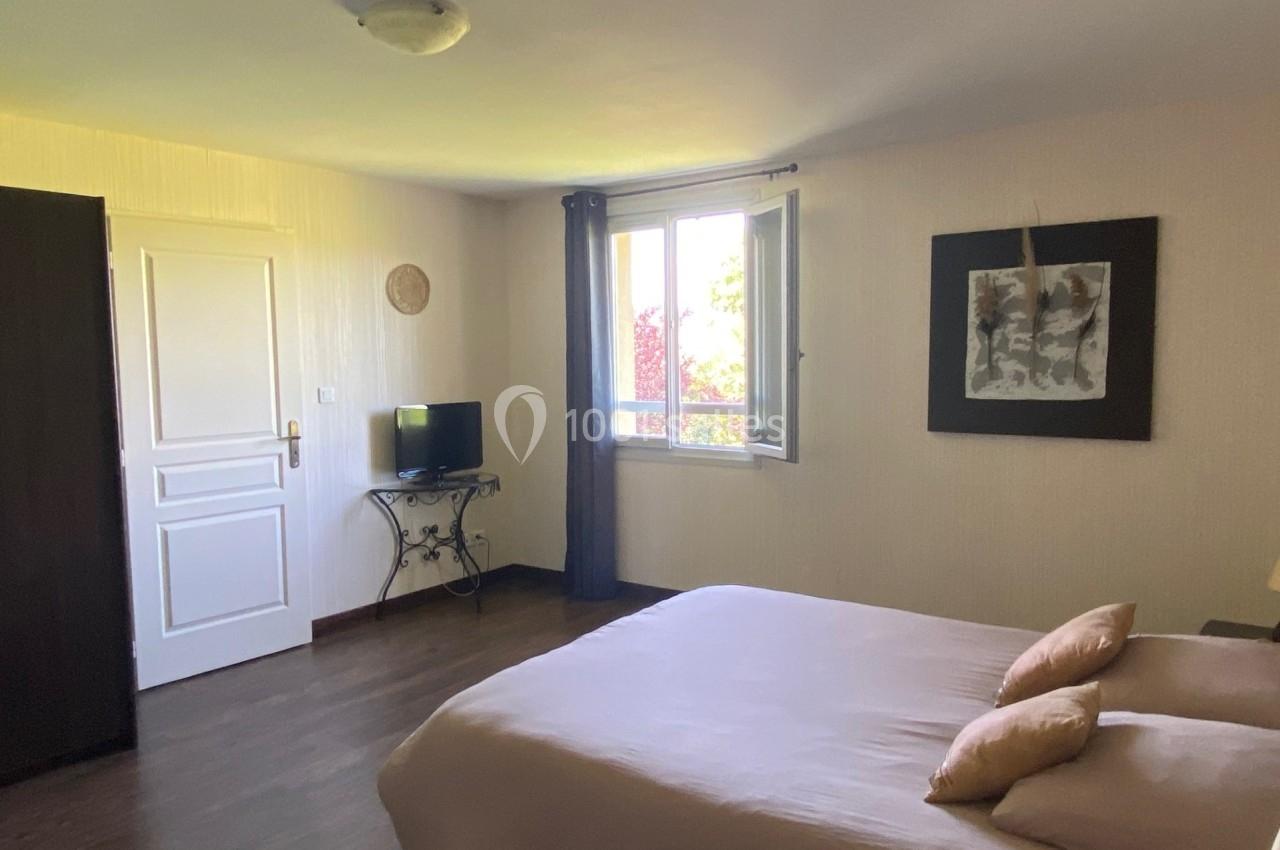 Chambre lumineuse avec lit double, armoire, téléviseur sur table et fenêtre donnant sur un extérieur verdoyant.