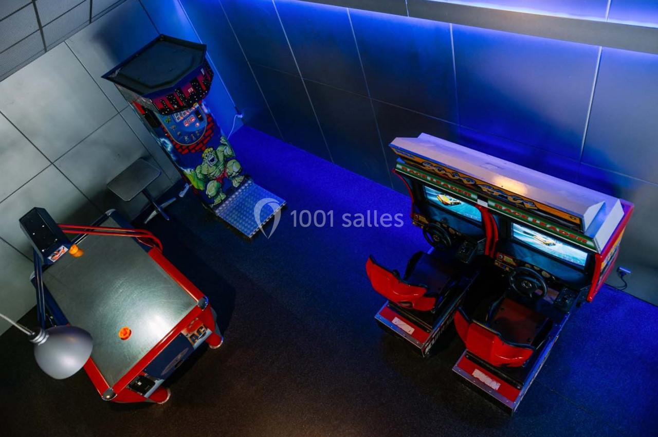 Salle de jeux avec une table de hockey sur air, une borne d'arcade et un simulateur de course, éclairée par des lumières…