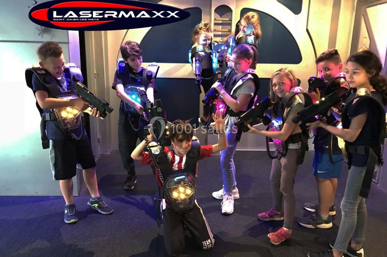 Des enfants équipés de gilets et pistolets lumineux jouent au laser game dans une salle aux décors futuristes.