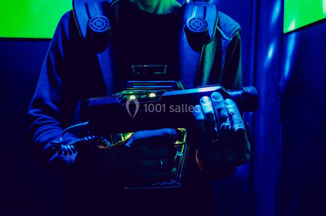 Personne tenant un pistolet laser dans un environnement sombre éclairé par des lumières bleues et vertes.