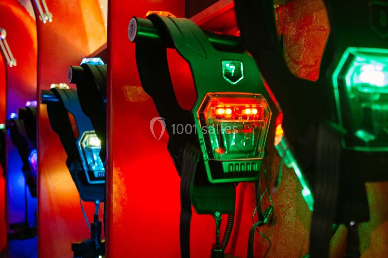 Équipements de laser game accrochés à un mur, éclairés par des lumières rouges et vertes.