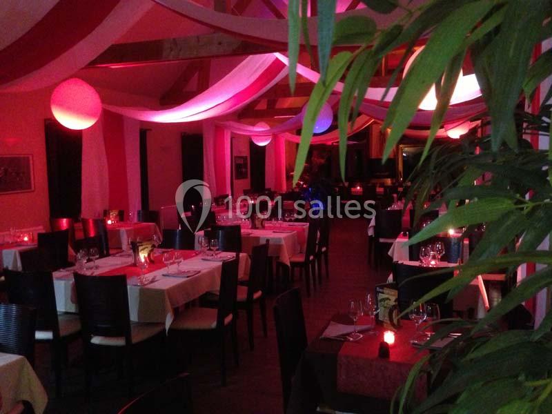 Salle de restaurant décorée avec des nappes blanches et rouges, éclairage tamisé et ambiance chaleureuse.