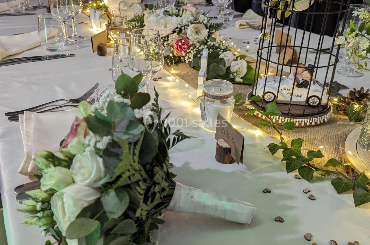 Table décorée pour un mariage avec fleurs, bougies, une cage ornée et un bouquet de mariée au premier plan.