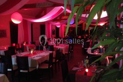 Salle de restaurant décorée avec des nappes blanches et rouges, éclairage tamisé et ambiance chaleureuse.