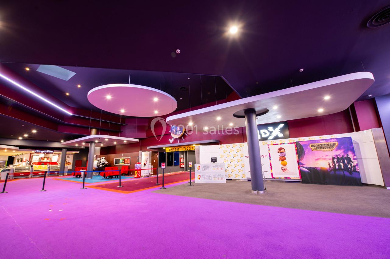 Hall d'entrée d'un cinéma avec comptoir de confiseries, affiches promotionnelles et éclairage coloré.