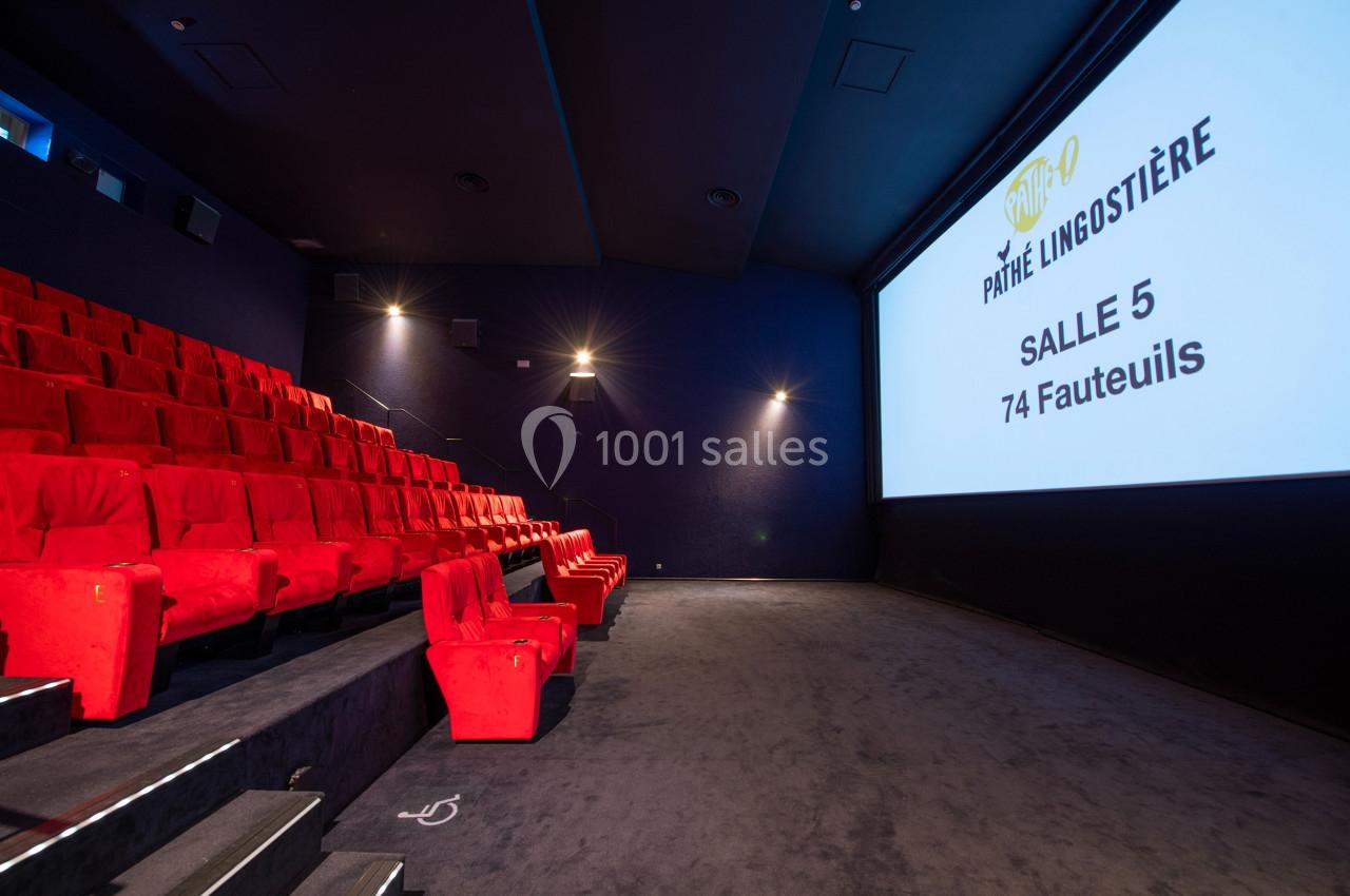 Salle de cinéma avec des sièges rouges, écran blanc affichant ’Salle 5, 74 fauteuils’ et éclairage tamisé.