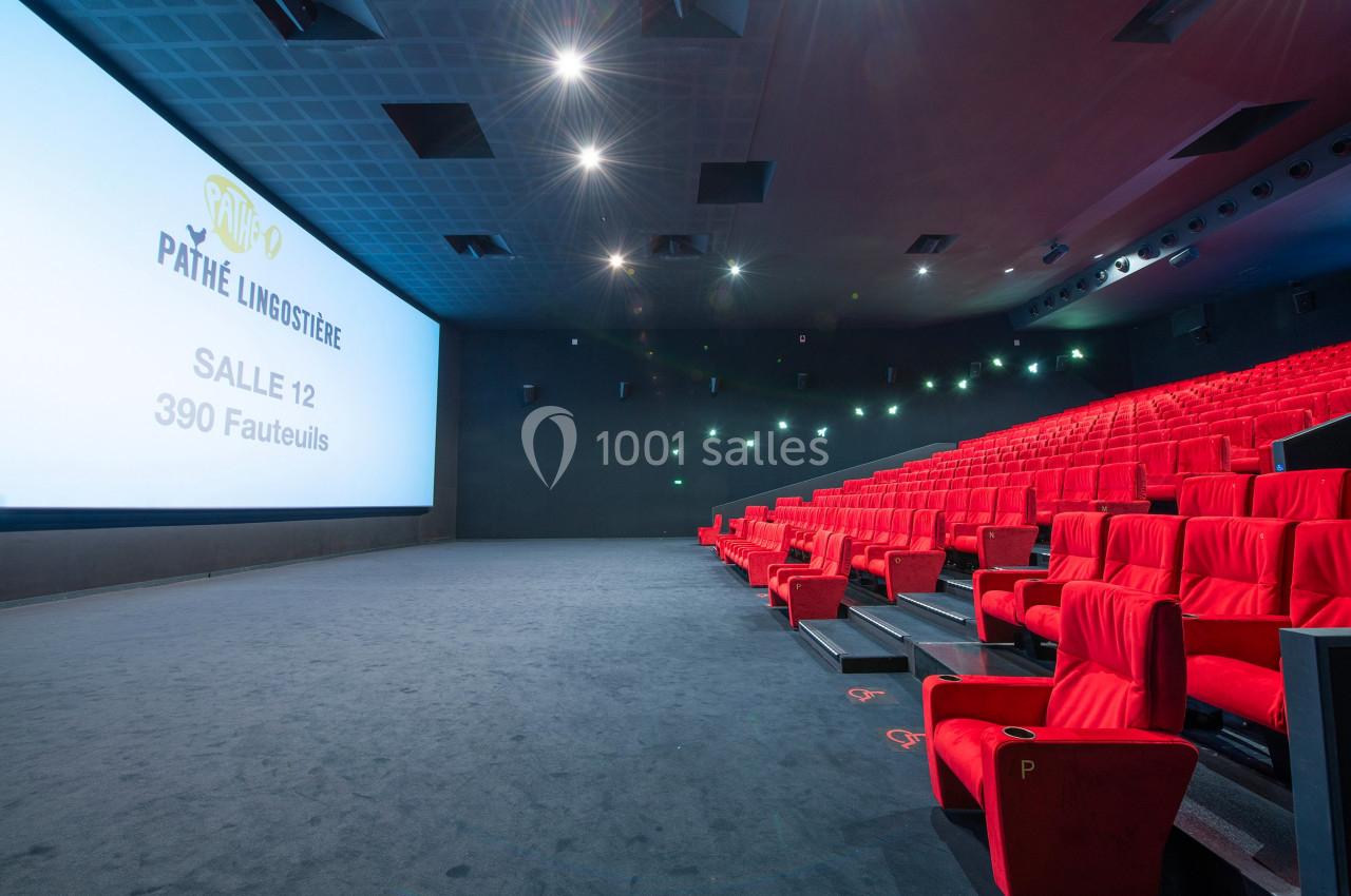 Salle de cinéma moderne avec écran géant, rangées de fauteuils rouges et éclairage tamisé.