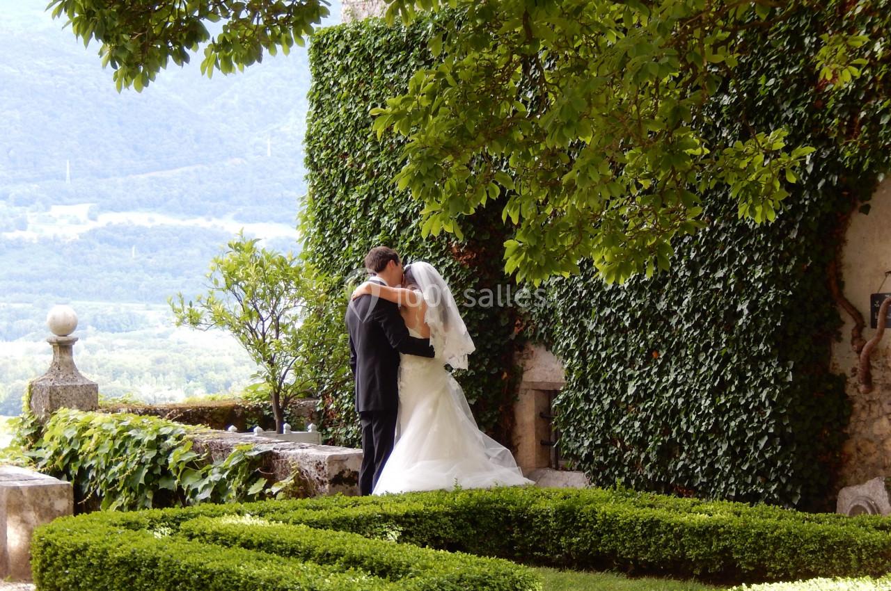 Un couple en tenue de mariage s'embrasse dans un jardin verdoyant près d'un mur couvert de lierre.