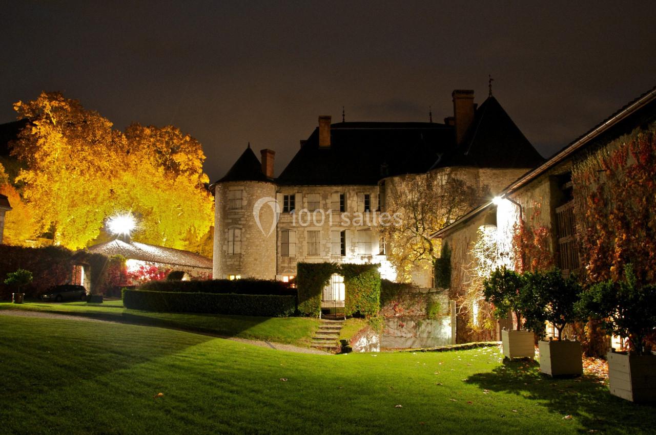 Château éclairé la nuit, entouré d'arbres aux feuilles automnales et d'une pelouse bien entretenue.