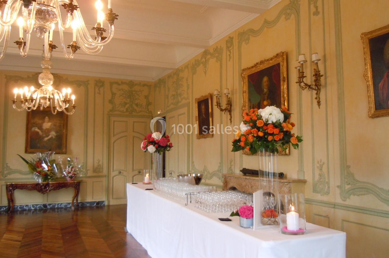 Salle élégante avec moulures, lustres, peintures anciennes et une table dressée avec verres et décorations florales.